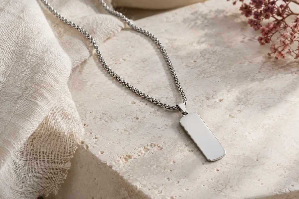Collier PROSTEEL argenté à chaîne spiga et pendentif plaque rectangulaire posé sur une surface claire.