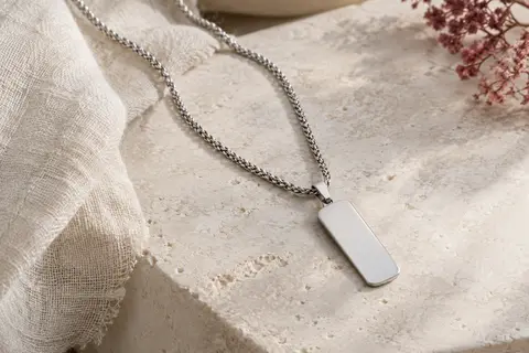 Collier PROSTEEL argenté à chaîne spiga et pendentif plaque rectangulaire posé sur une surface claire.