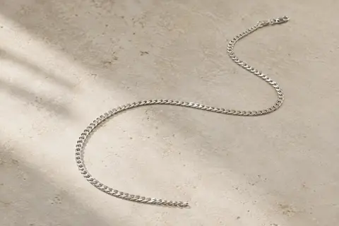 Chaîne gourmette en argent 925 aux maillons plats, disposée seule sur une surface claire