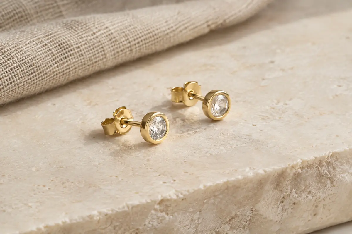 Paire de puces d’oreilles dorées avec pierre transparente de 4 mm sur une surface ivoire