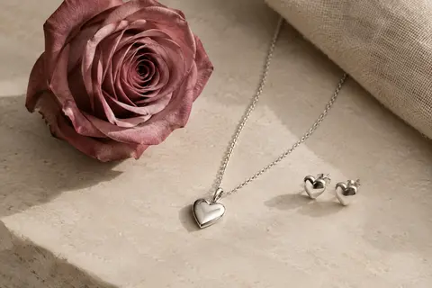 Rose préservée, collier argenté à pendentif cœur et boucles d’oreilles disposés sur une surface claire.