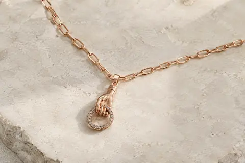 Collier de ton or rosé avec pendentif en forme de main tenant un cercle pavé de cristaux