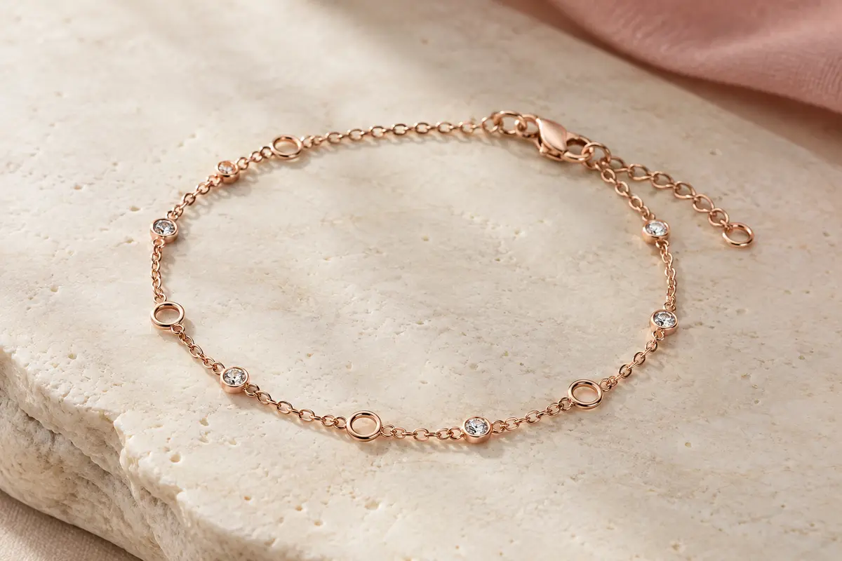 Bracelet chaîne ton or rose avec cristaux ronds espacés et fermoir mousqueton, posé sur une surface claire.