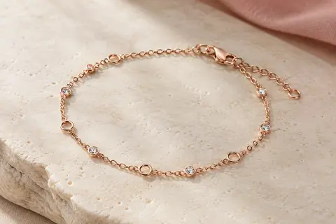 Bracelet chaîne ton or rose avec cristaux ronds espacés et fermoir mousqueton, posé sur une surface claire.