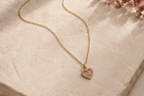 Collier TINGN doré avec pendentif cœur à initiale et chaîne fine posé sur une surface claire.