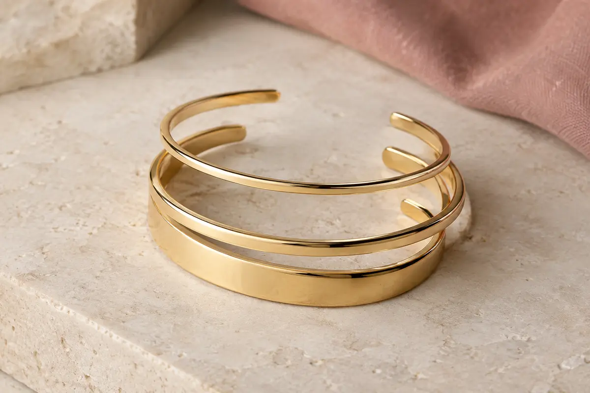 Trois bracelets joncs ouverts en acier inoxydable doré, présentés seuls sur une surface claire
