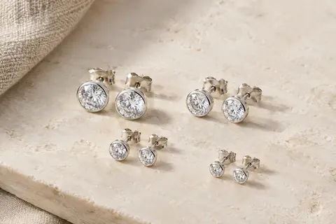 Quatre paires de puces d’oreilles argentées ornées de zircones transparentes, disposées sur une surface claire.