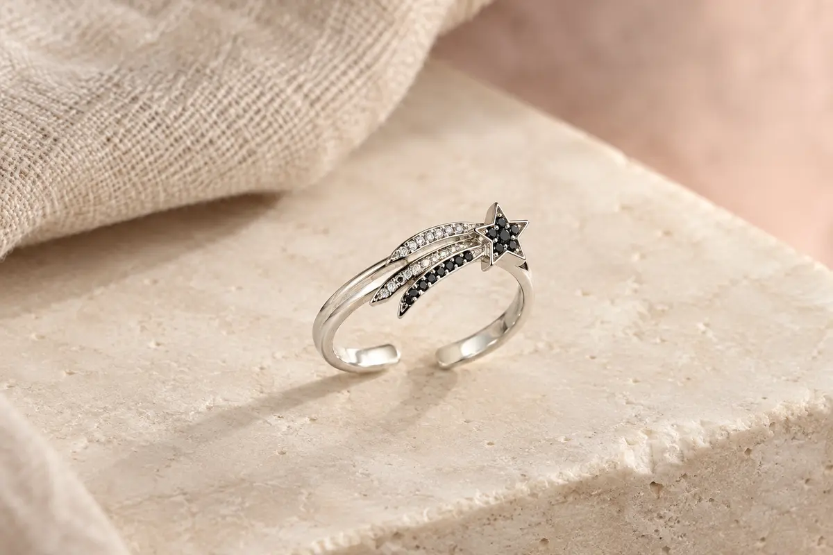 Bague ouverte Yumilok en argent 925, motif étoile filante avec zircone noire et claire, posée sur une surface ivoire.